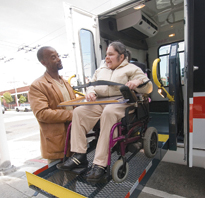 photo of paratransit van operator and woman in wheelchair using lift to enter paratransit van