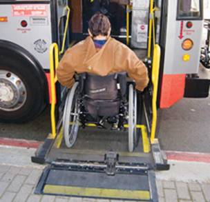 Photograph of person in manual wheelchair using a wheelchair lift on Muni high floor bus.
