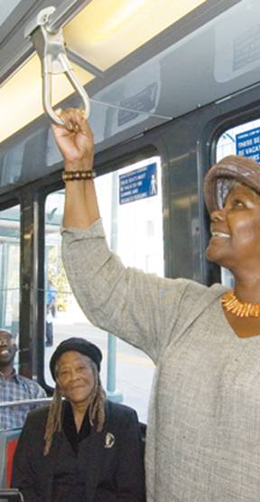 Photograph of woman standing on crowded Muni vehicle using overhead handhold.